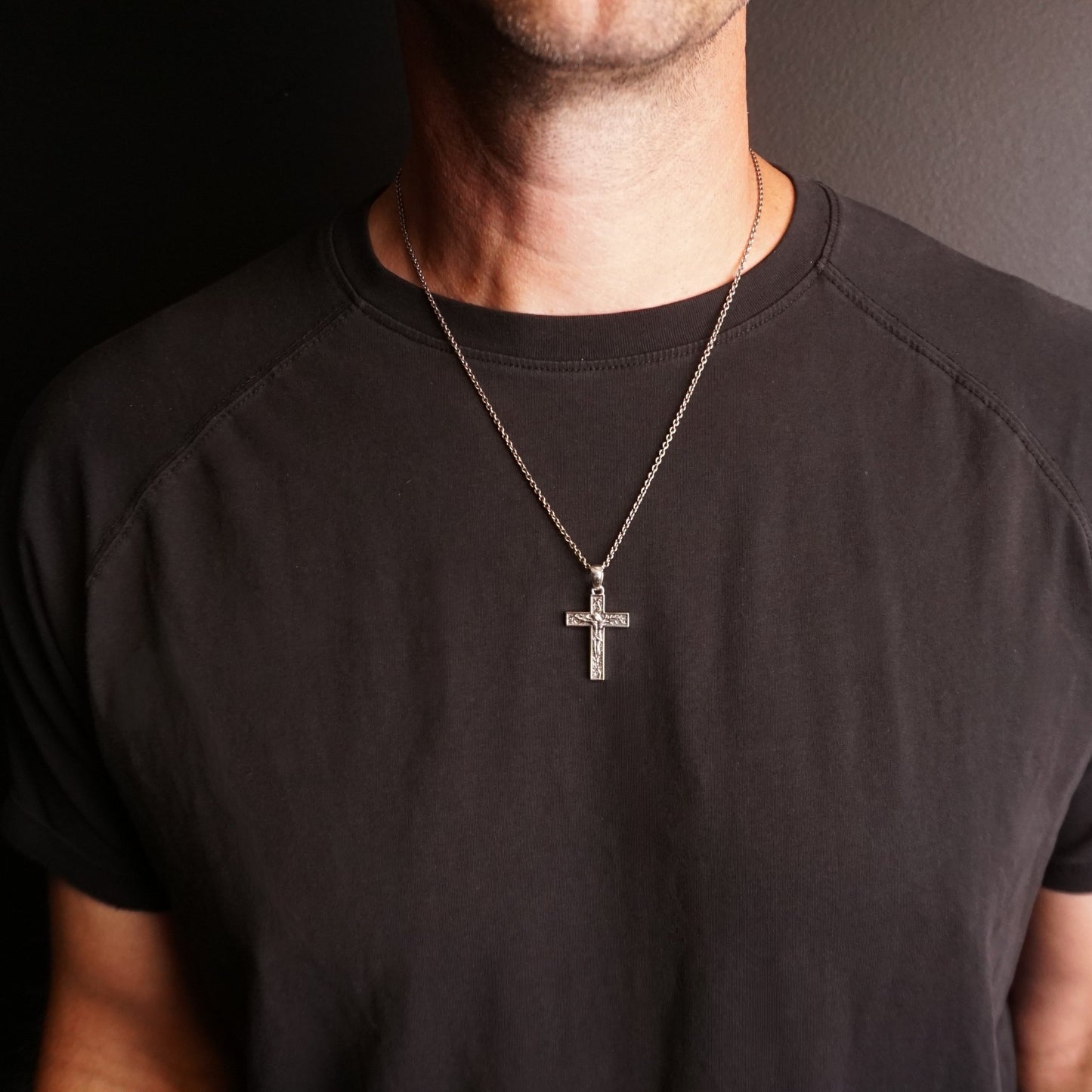 Person wearing a black t-shirt with a crucifix pendant necklace against a dark background